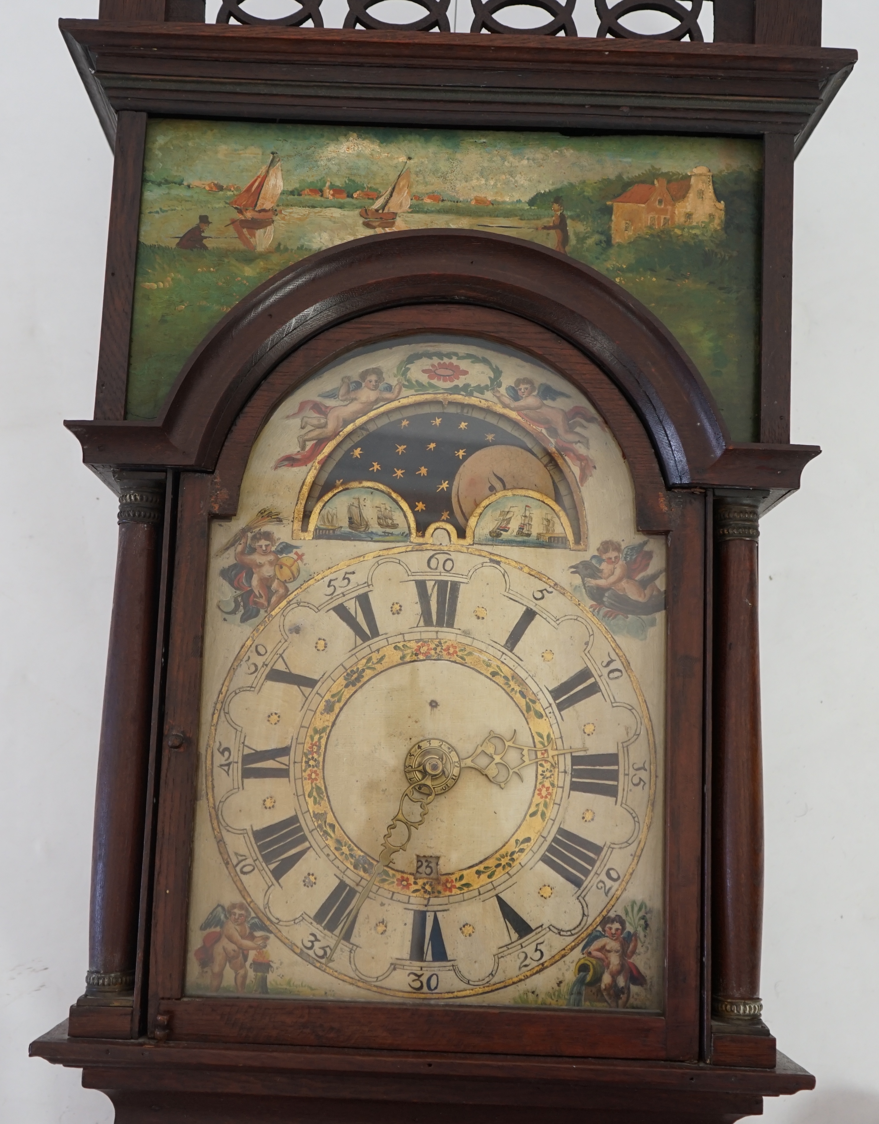 A late 18th century Dutch Frisian Staart oak eight day wall clock, with atlas and angel finials, hood painted with a Dutch riverscape and painted arched dial with moonphase, date aperture and alarm indicator, 47cm wide,